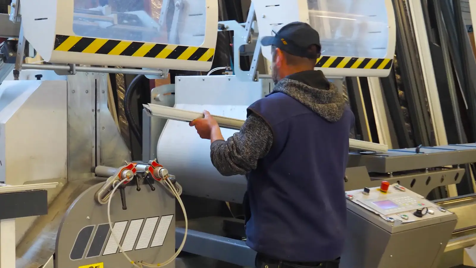 Un menuisier engage un profilé dans une machine de coupe de l’atelier