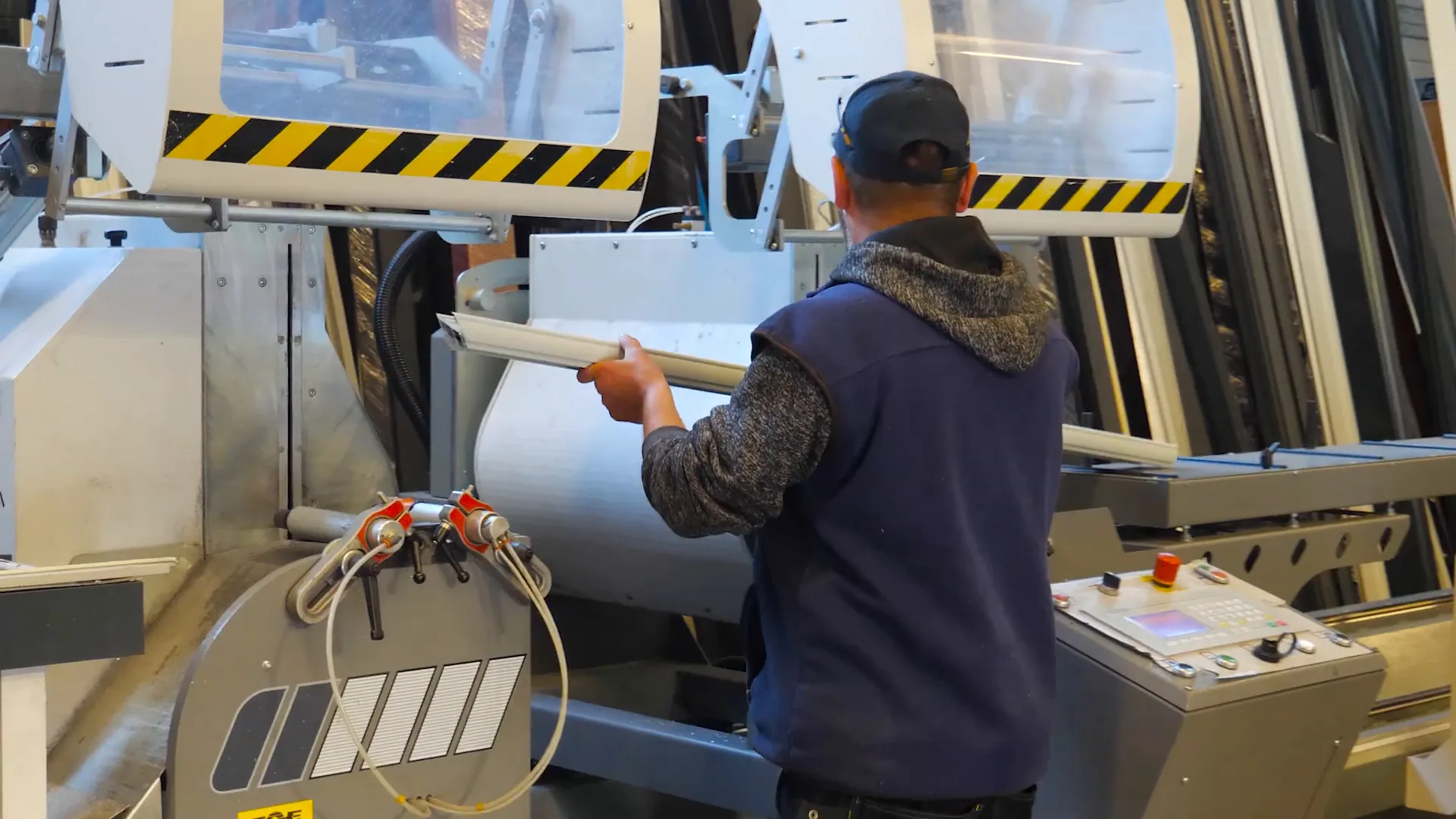 Un menuisier engage un profilé dans une machine de coupe de l’atelier