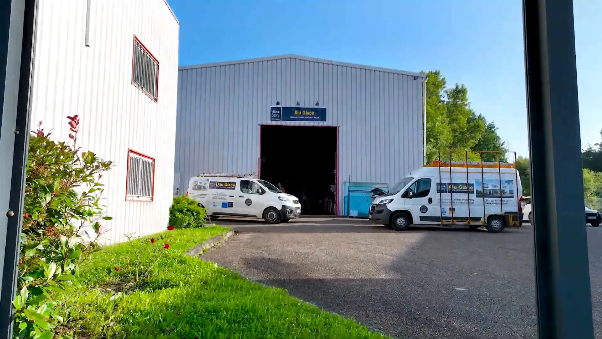 Bâtiment de l’atelier Alu Glace à Vierzon, grande porte ouverte, deux camionnettes blanches