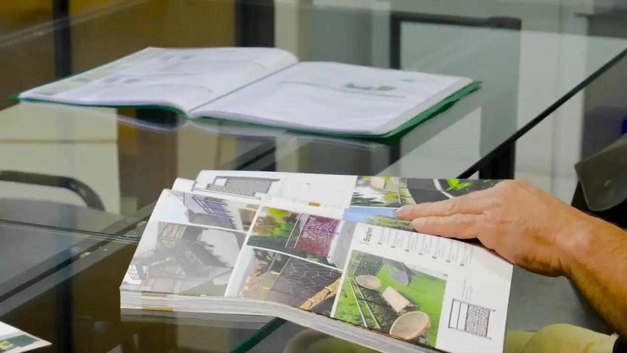 Une main feuillette un catalogue ouvert sur une table en verre