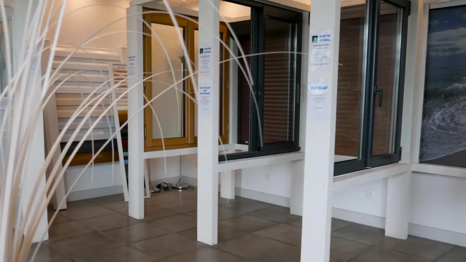 Fenêtres exposées dans le showroom, châssis gris et teinte bois, avec leurs affichettes
