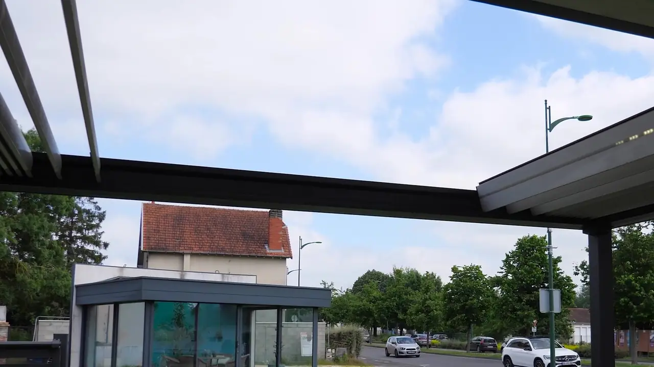 Structure de pergola grise vue de dessous, lames ouvertes, véranda au fond