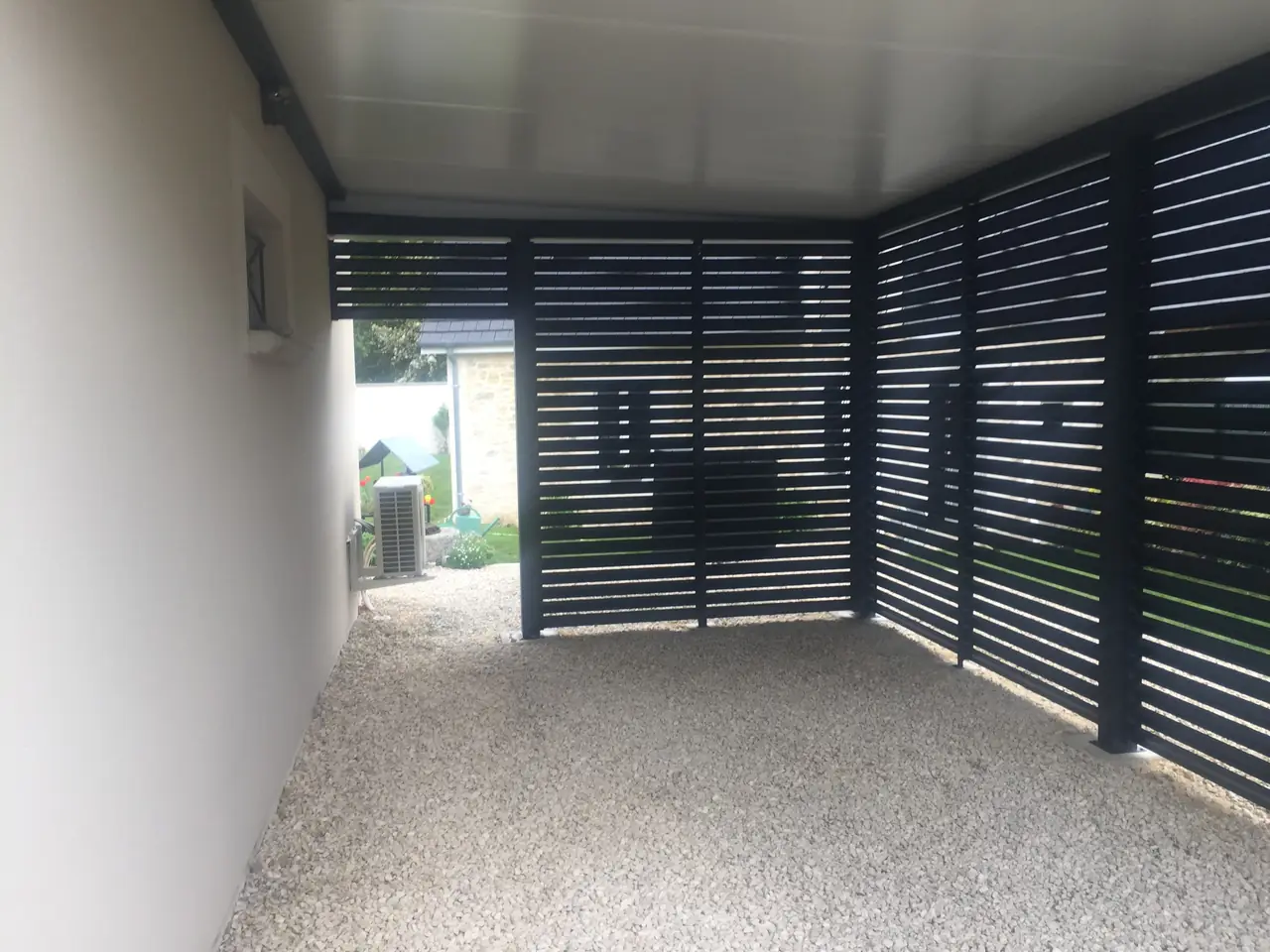 Intérieur d’un abri aux parois de lames horizontales gris anthracite, sol gravillonné