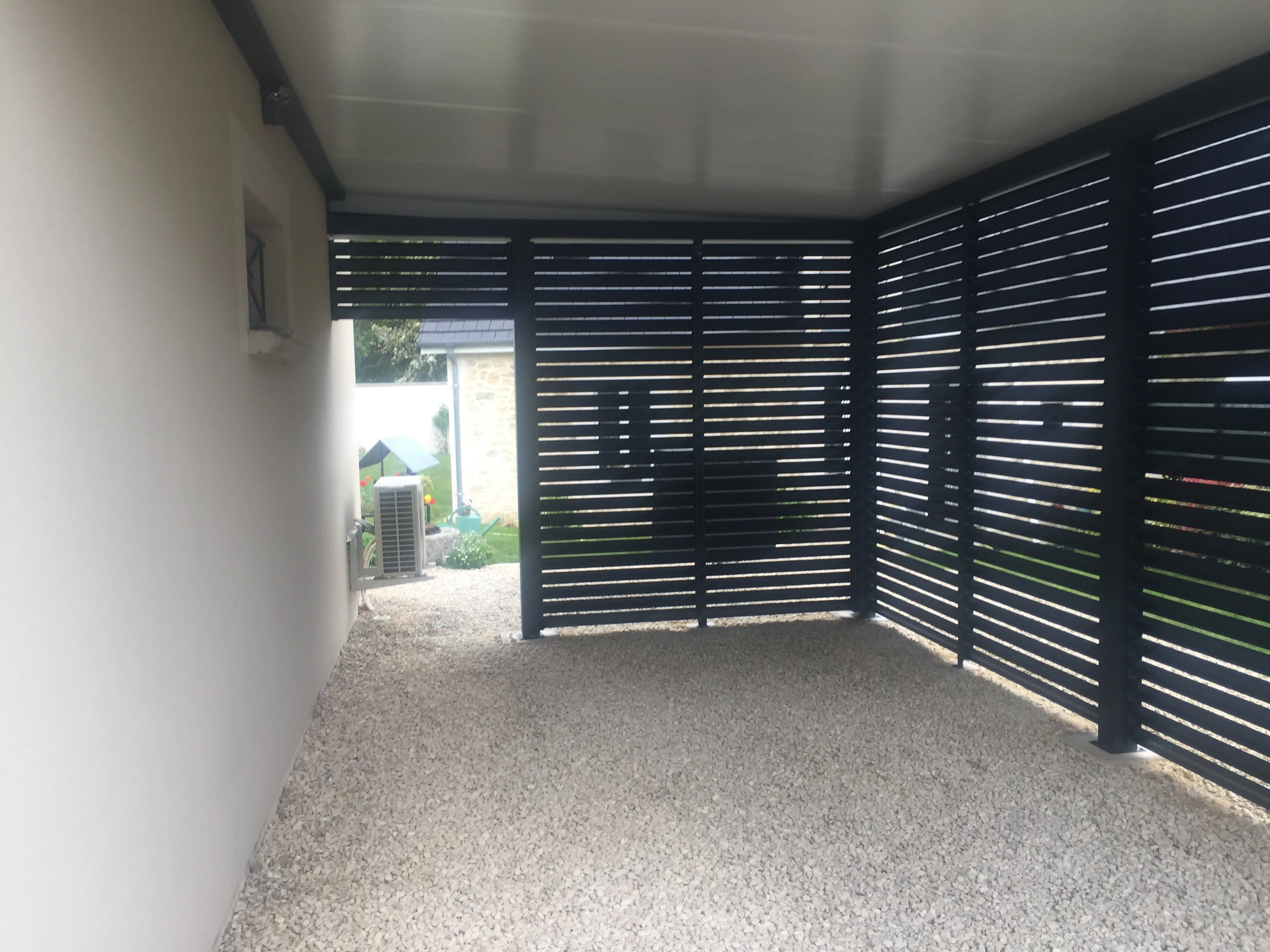 Intérieur d’un abri aux parois de lames horizontales gris anthracite, sol gravillonné