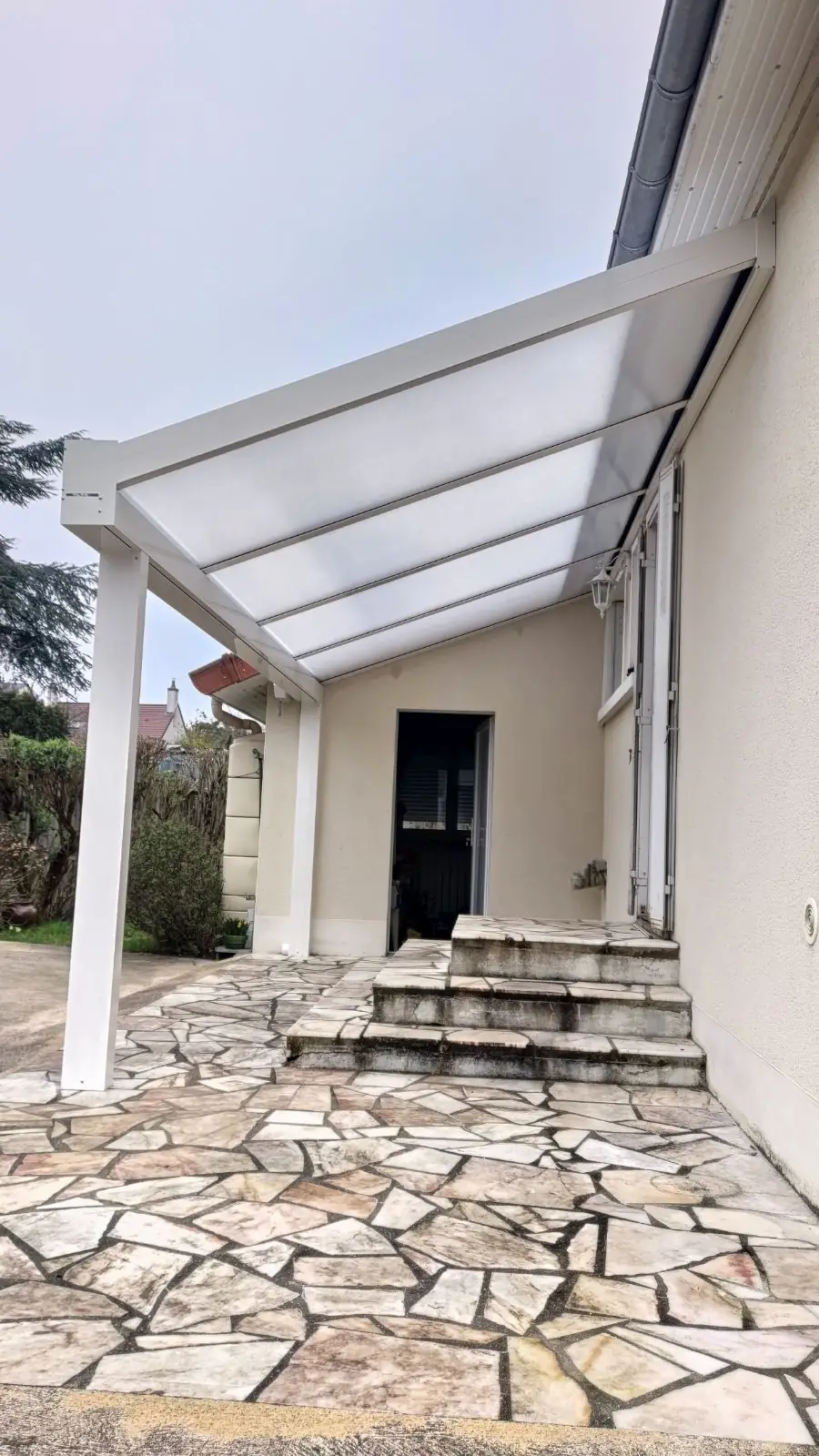 Auvent blanc à couverture translucide sur poteaux au-dessus d’un escalier d’entrée