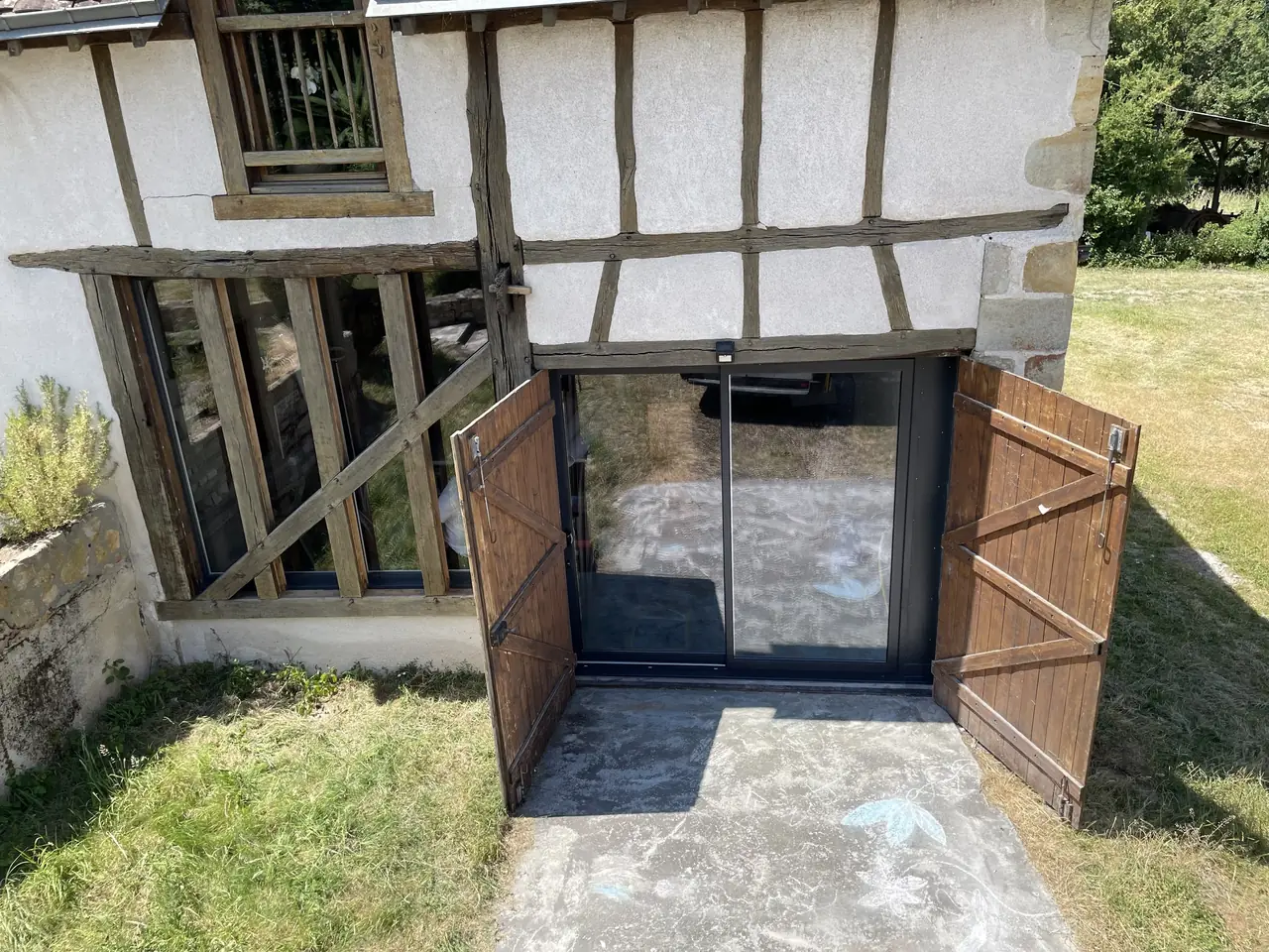 Baie coulissante gris anthracite posée dans une façade à colombages, volets en bois ouverts de part et d’autre