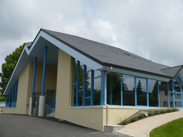 Bâtiment aux grandes baies et poteaux bleus sous un toit à deux pentes