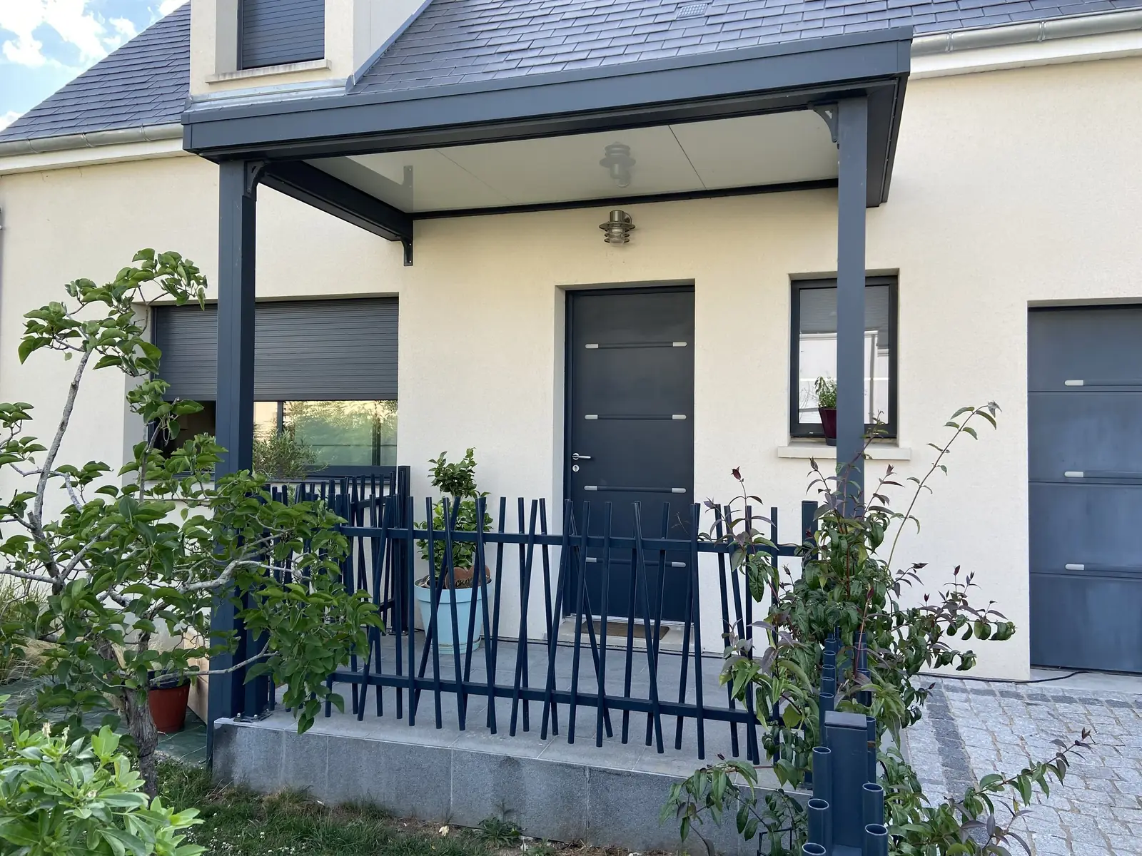 Entrée de maison sous une marquise gris anthracite sur poteaux, porte d’entrée et barrière assorties