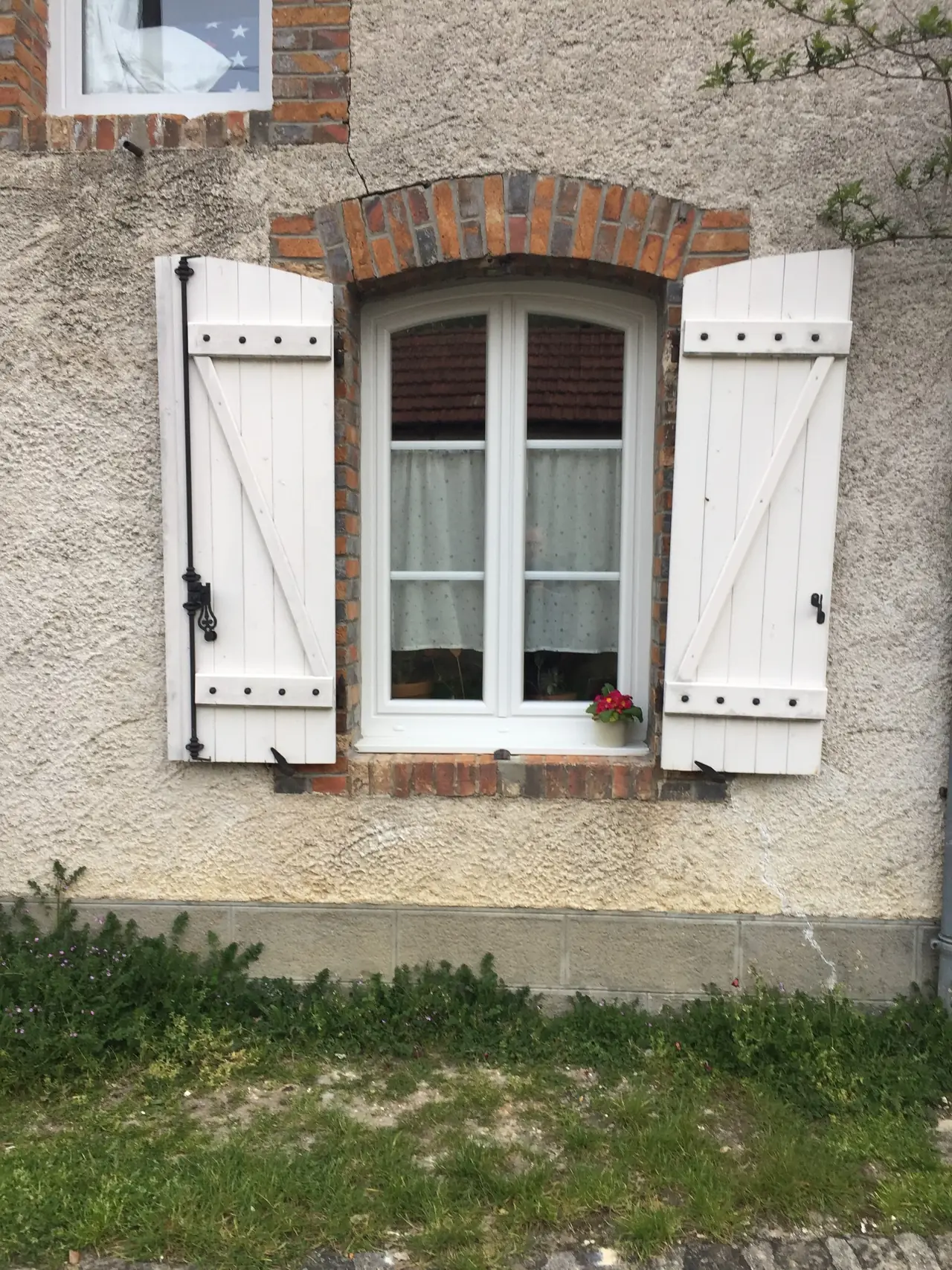 Fenêtre blanche à deux vantaux sous un arc de briques, volets battants blancs