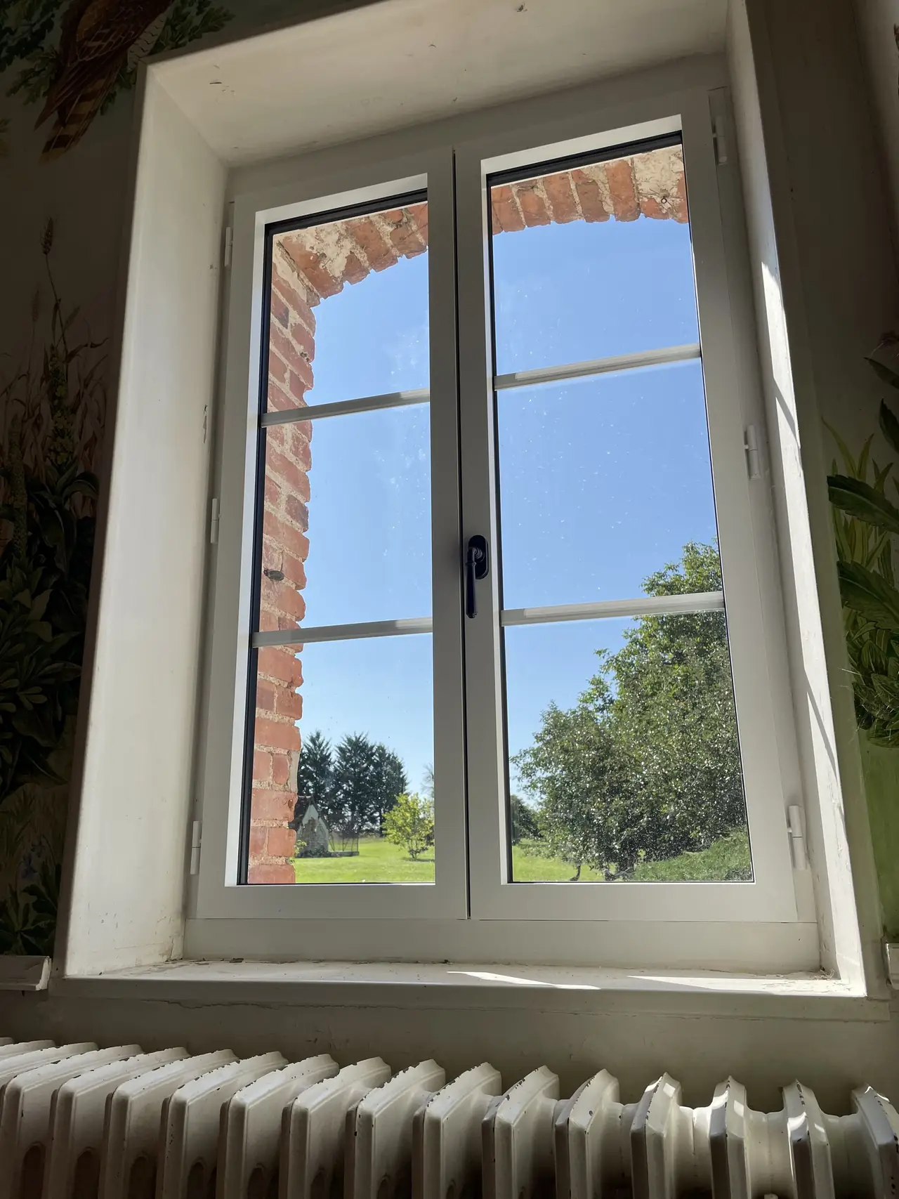 Fenêtre blanche à petits bois vue de l’intérieur, tableau en briques, radiateur en fonte