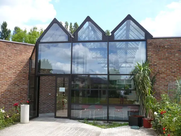 Façade vitrée à trois pignons et porte d’entrée entre deux murs de briques