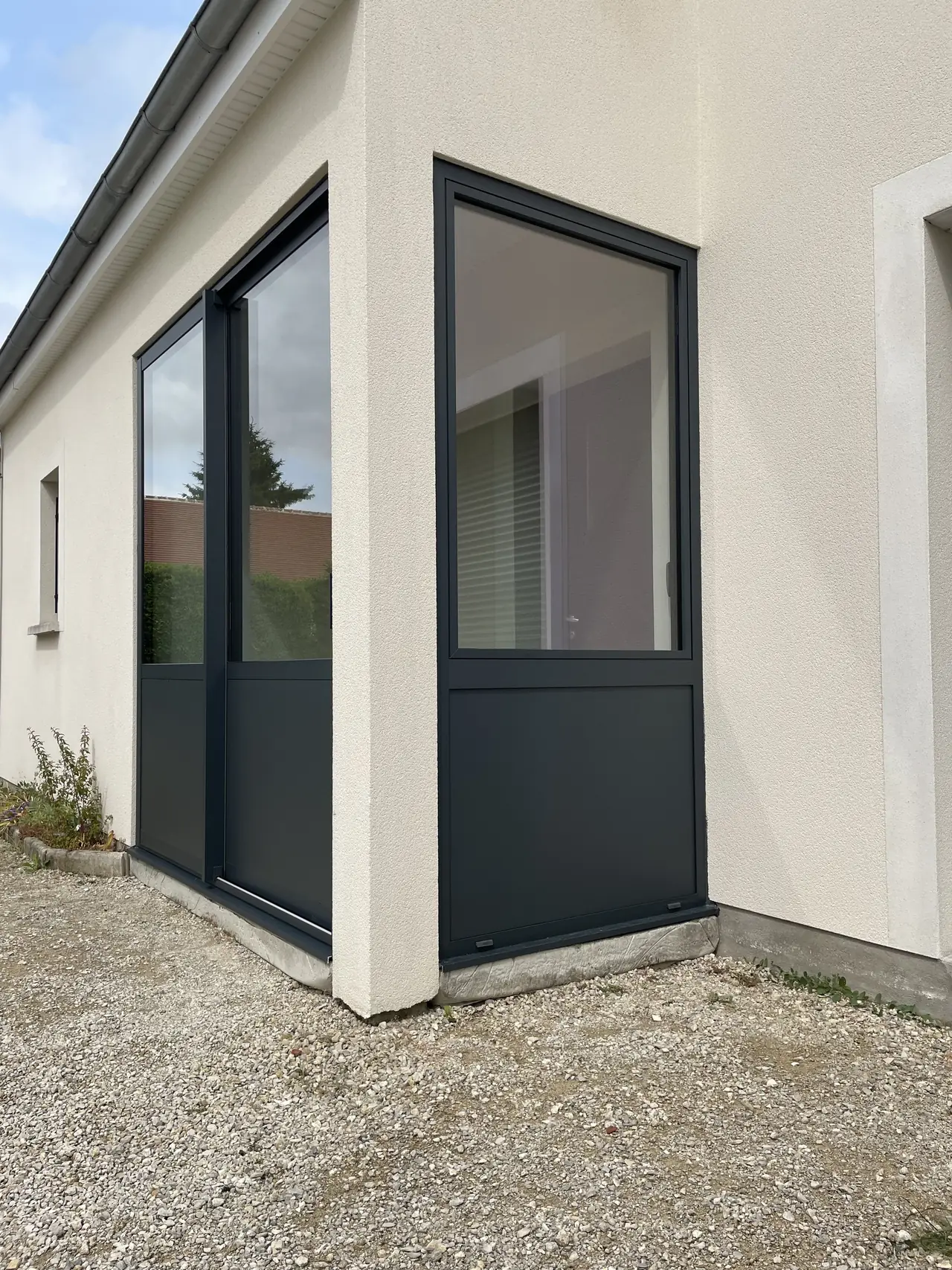 Deux menuiseries gris anthracite vitrées en partie haute, à l’angle d’une maison
