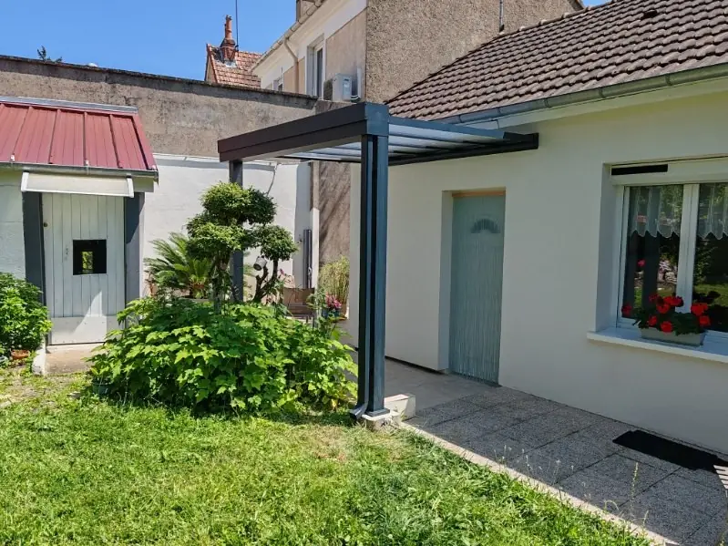 Pergola gris anthracite adossée à une maison, au-dessus d’une allée de jardin