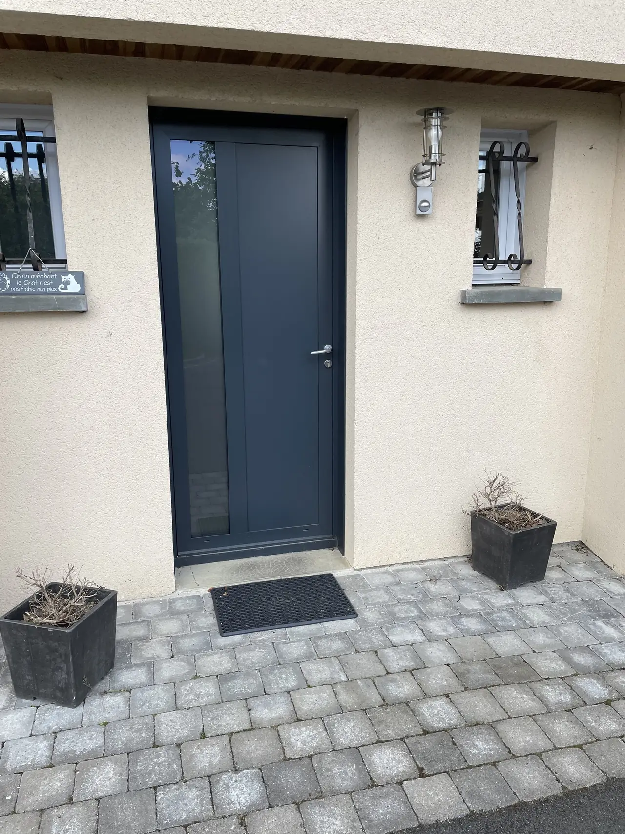 Porte d’entrée gris anthracite à bande vitrée verticale, entre deux fenêtres à barreaux