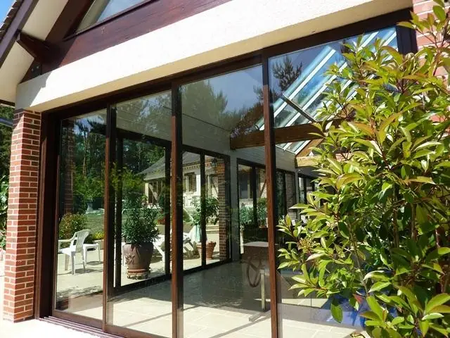 Grandes baies vitrées coulissantes sous une toiture vitrée, jardin en reflet