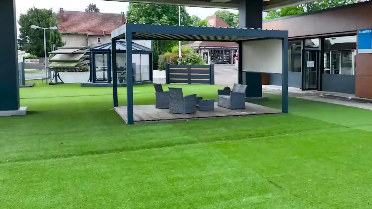 Exposition extérieure d’Alu Glace à Saint-Doulchard : pergola avec salon de jardin, véranda, stores et clôtures sur gazon