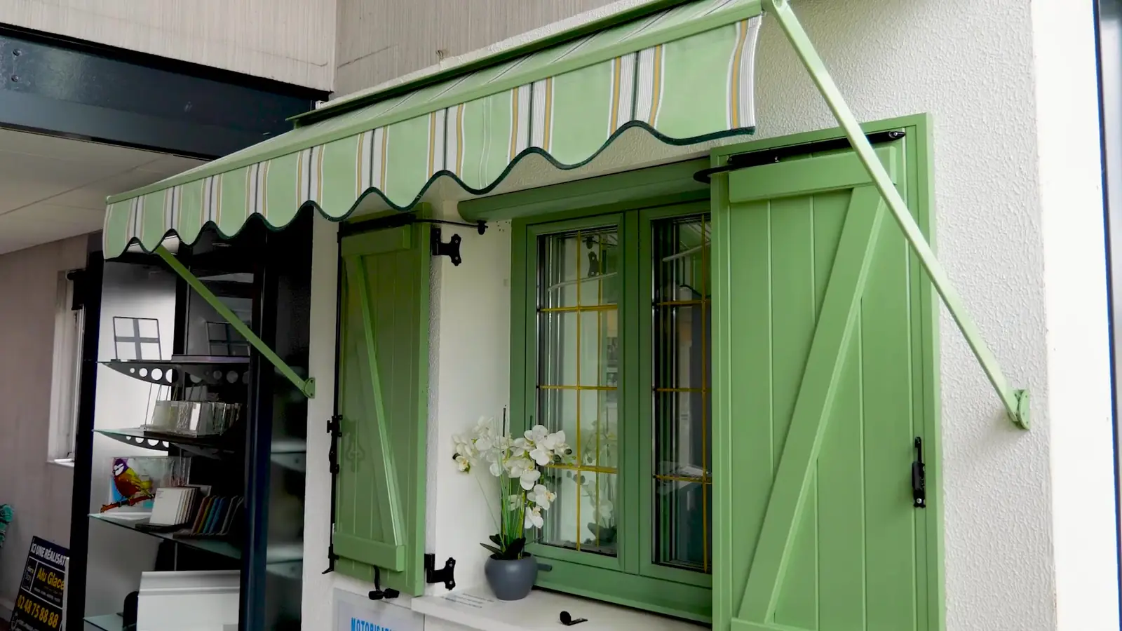 Fenêtre verte à petits bois, volets battants verts et store banne rayé vert et blanc à lambrequin