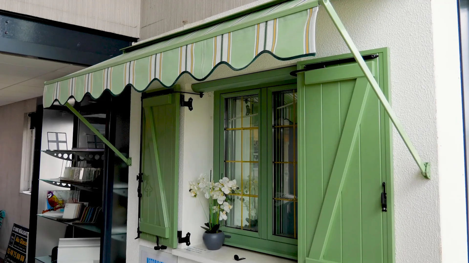 Fenêtre verte à petits bois, volets battants verts et store banne rayé vert et blanc à lambrequin